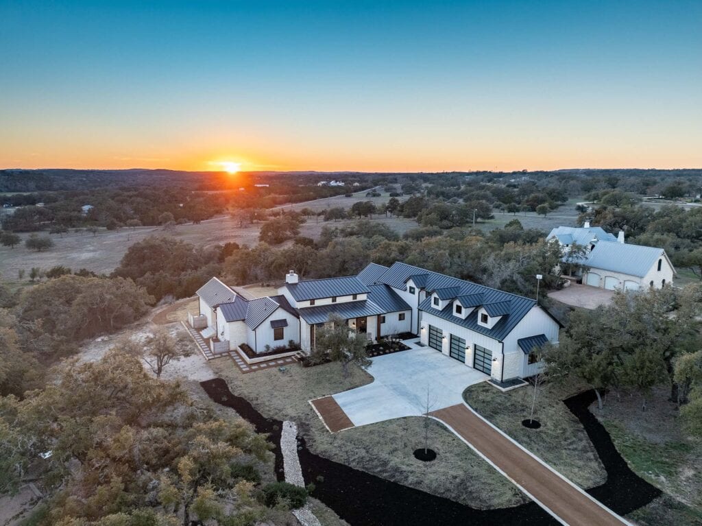 Modern house with a large driveway and surrounding trees at sunset.